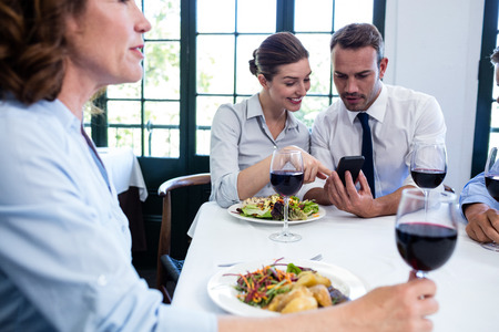 Business colleagues looking at mobile phone during business lunch meeting at restaurantの写真素材