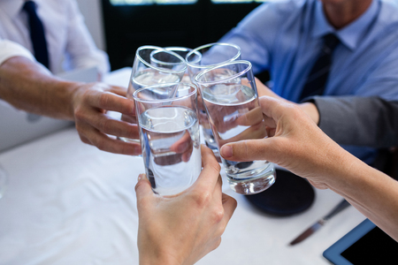 Group of businesspeople toasting glass of water during business meeting in restaurantの写真素材