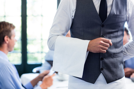 Close-up of waiter standing with napkin in restaurantの写真素材