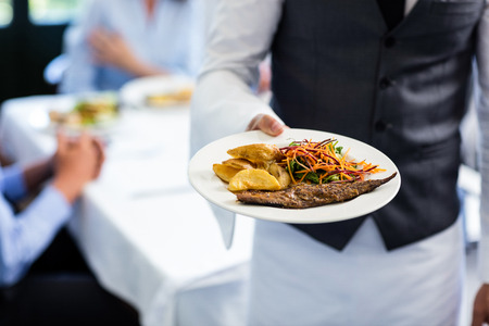 Close-up of waiter holding plate of meal in restaurantの写真素材