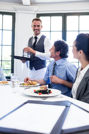 Waiter serving water to the business people in restaurantの写真素材