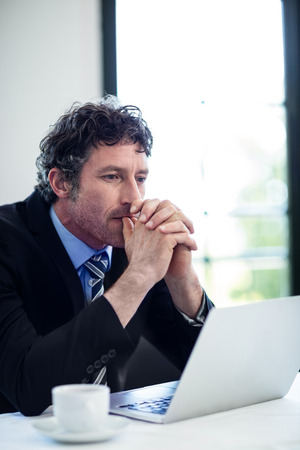Close-up of thoughtful businessman sitting in restaurant in front of laptopの写真素材