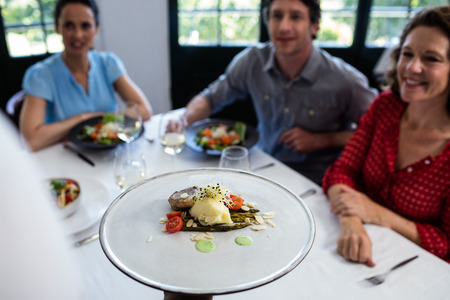 Waiter serving meal to group of friends in a restaurantの写真素材