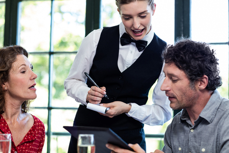 Young waitress taking an order from a couple at restaurantの写真素材
