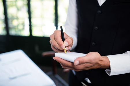 Close-up of waiter taking an order wearing a waistcoat in a restaurantの写真素材