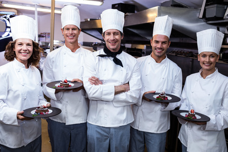 Happy chefs presenting their dessert plates in commercial kitchenの写真素材