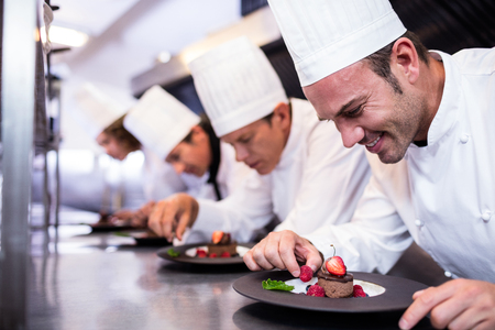 Team of chefs finishing dessert plates in the kitchenの写真素材