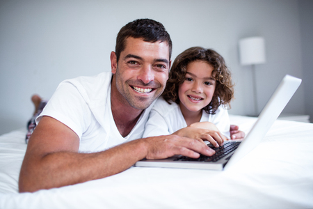 Portrait of father and son using laptop on bed in bedroomの写真素材