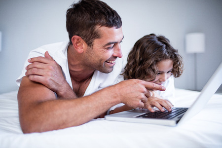 Father and son using laptop on bed in bedroomの写真素材