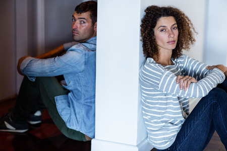 Portrait of couple sitting on opposite sides of the wall and feeling sad