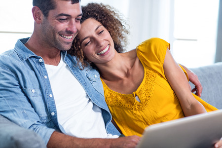 Young couple sitting on sofa and using laptop in living roomの写真素材