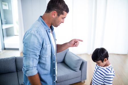 Angry father scolding his son in living room at homeの写真素材