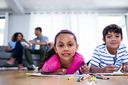 Portrait of brother and sister drawing and parents sitting on sofa in backgroundの写真素材