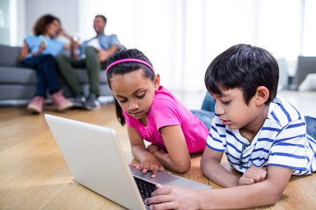 Brother and sister using laptop while parents sitting on sofa in backgroundの写真素材