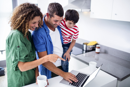Parents using laptop with son in kitchen at homeの写真素材