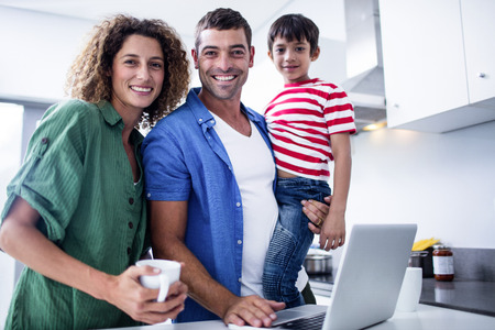 Parents using laptop with son in kitchen at homeの写真素材