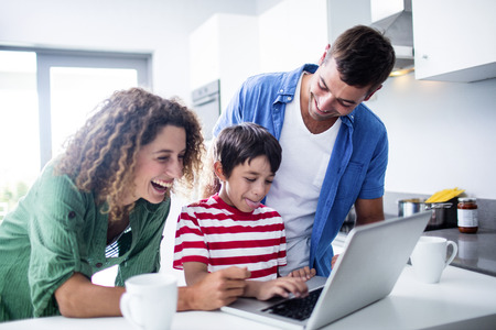 Parents using laptop with son in kitchen at home