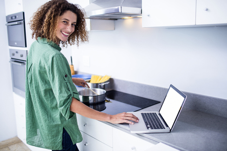 Portrait of woman working on laptop while cooking in kitchenの写真素材