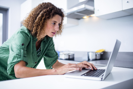 Woman working on laptop in kitchen at homeの写真素材