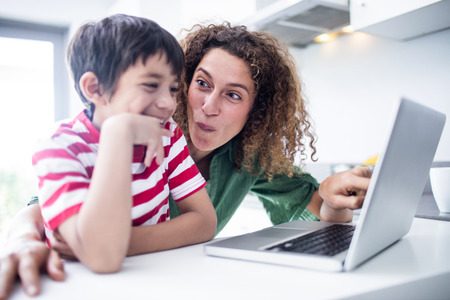 Mother and son using laptop in kitchen at homeの写真素材