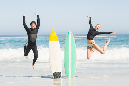 Excited couple jumping next to surfboards on the beach