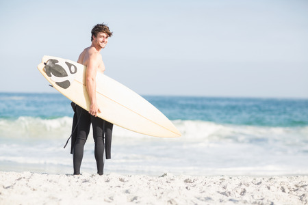 Happy surfer walking on the beach with a surfboard