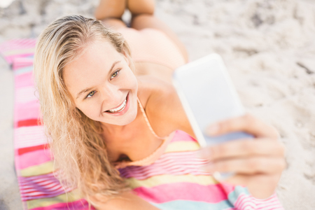 Pretty woman in bikini lying on the beach and taking a selfie on phoneの写真素材