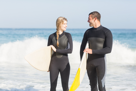Couple with surfboard walking on the beach on a sunny dayの写真素材