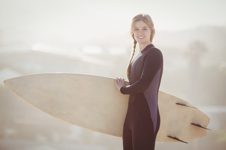 Happy woman in wetsuit holding a surfboard on the beach on sunny day
