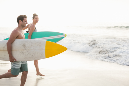Couple with surfboard running on the beach on a sunny dayの写真素材