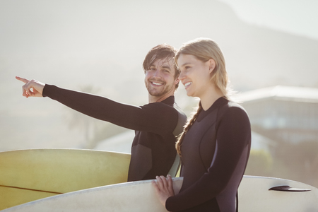 Couple with surfboard standing on the beach on a sunny dayの写真素材