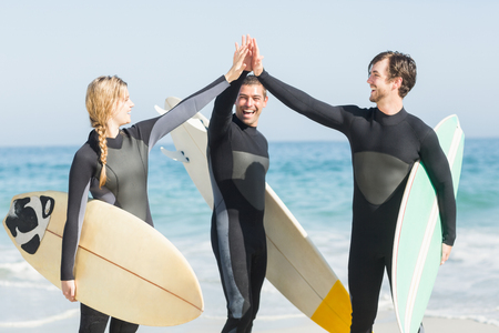 Happy surfer giving high-five to each other on the beach on a sunny dayの写真素材