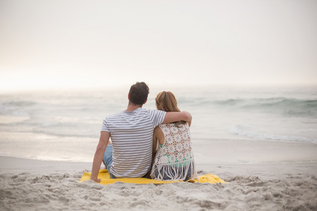 Rear view of couple sitting together on the beachの写真素材