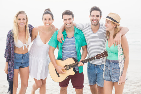 Group of friends standing on the beach with a guitar and looking at camera