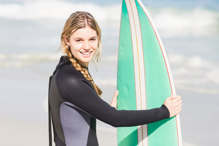 Portrait of woman in wetsuit holding a surfboard on the beach on a sunny day