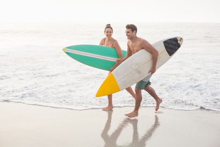 Couple with surfboard running on the beach on a sunny dayの写真素材