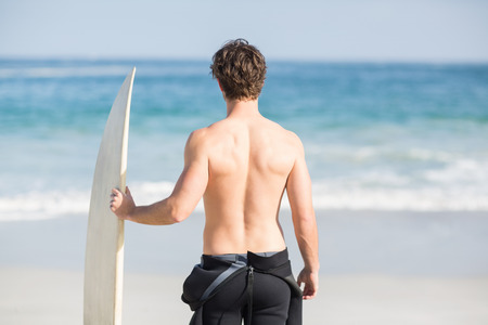Rear view of man with surfboard standing on the beach on a sunny day