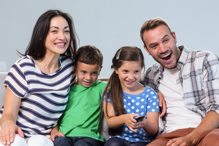 Happy family watching television with their two children sitting on a sofa in the living roomの写真素材