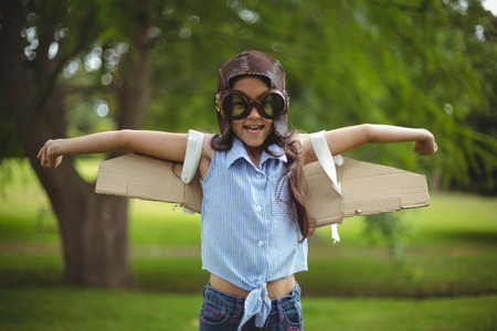 Young girl wearing leather pilot helmet and wings pretending to fly in gardenの写真素材