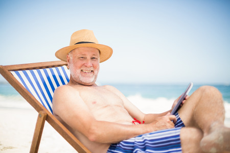 Senior man using tablet at the beach on a sunny dayの写真素材