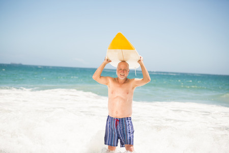 Senior man carrying surfboard on a sunny day