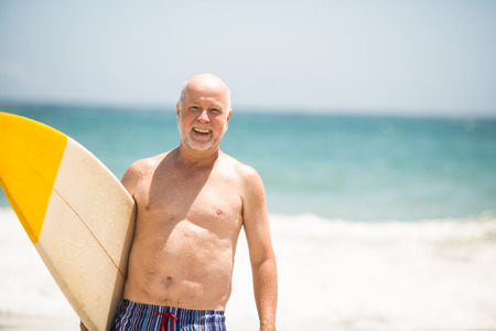 Senior man carrying surfboard on a sunny dayの写真素材