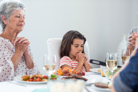 Family sitting at dining table and praying together before mealの写真素材