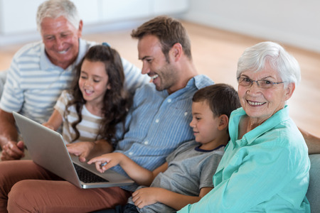 Happy family sitting on sofa using a laptop in living roomの写真素材