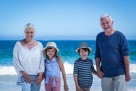 Cute children holding grandparents hands on the beach
