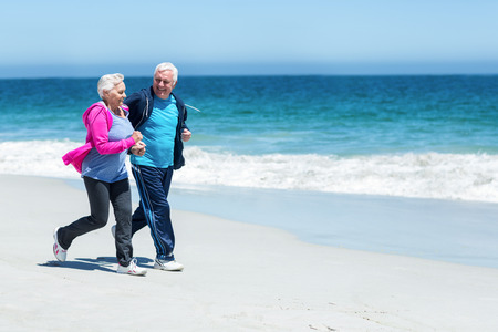 Cute mature couple running together on the beachの写真素材