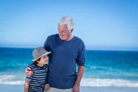 Cute boy embracing his grandfather on the beachの写真素材