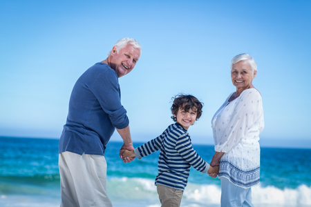 Cute boy holding his grandparents hands on the beachの写真素材