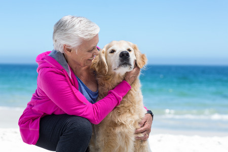 Cute mature woman petting her dog on the beachの写真素材
