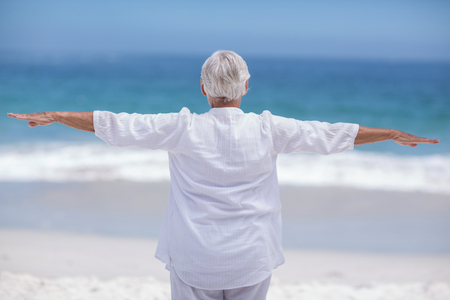Rear view of mature woman posing with outstretched arms at the beachの写真素材